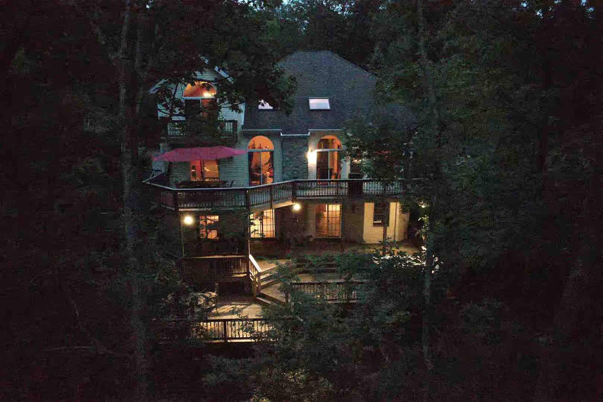 The house glowing warmly at night among dark trees